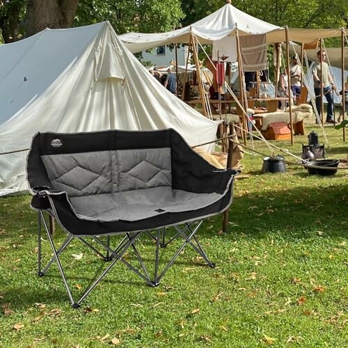 Double camping chair on grass with tents and people in background.
